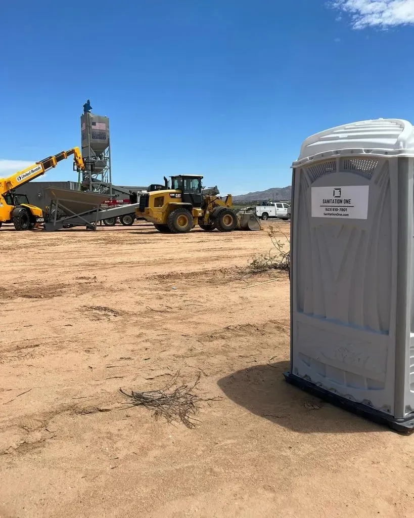 Sanitation One portable toilet at a desert construction site with heavy equipment